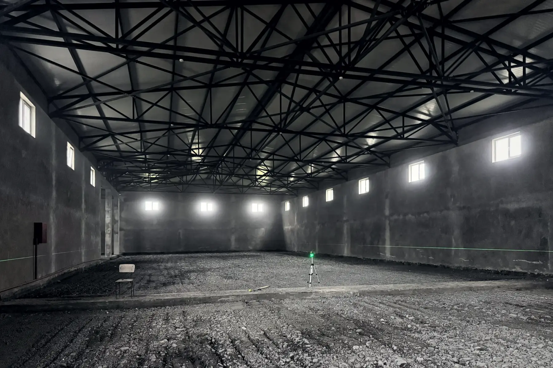 Steel roof trusses over the main hall, with a laser level set up on the compacted floor base